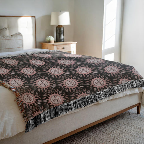 Luxurious woven cotton throw featuring dreamy blush pink sun faces with closed eyes against black background with delicate ray patterns and elegant fringe trim. Perfect celestial wall hanging, witchy bedroom decor, or dark academia throw blanket.